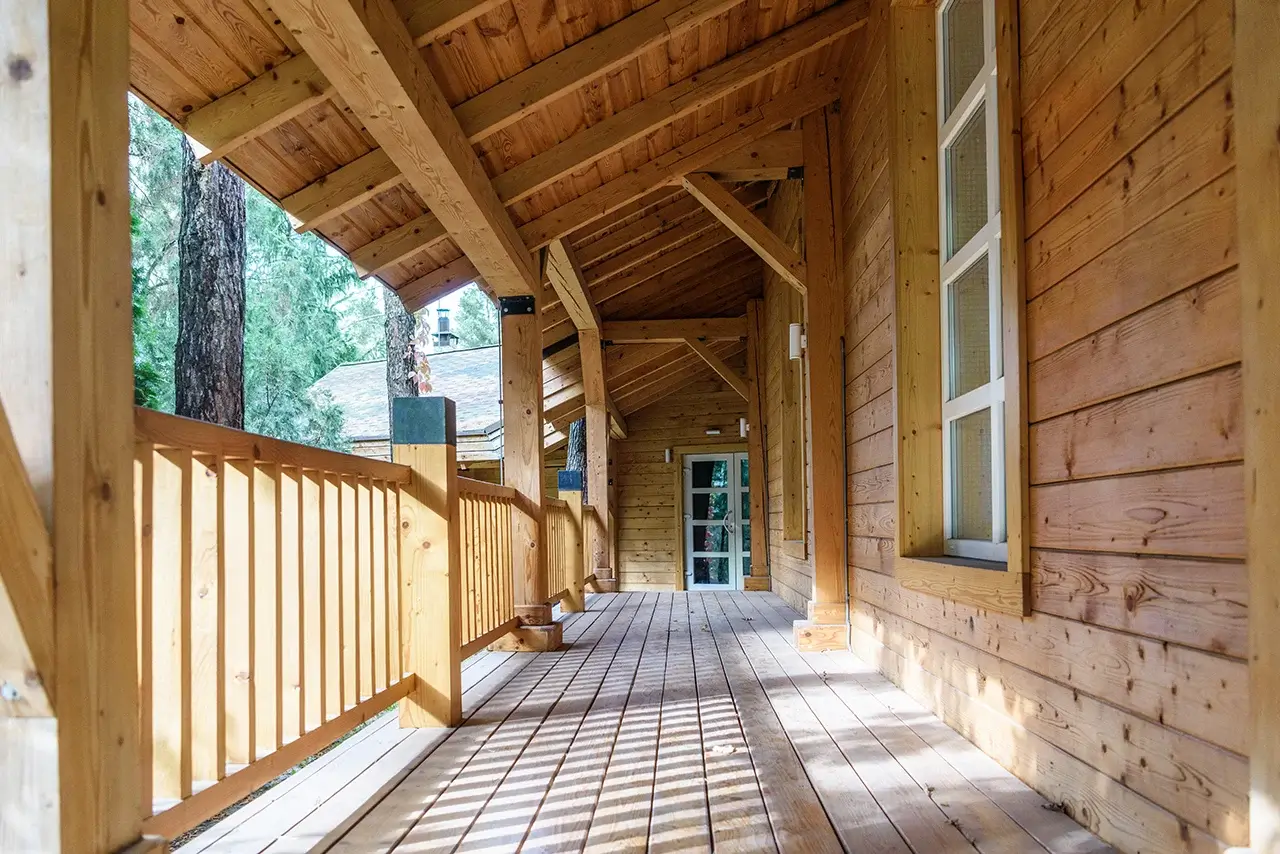 A rustic wooden porch of a lodge surrounded by trees.