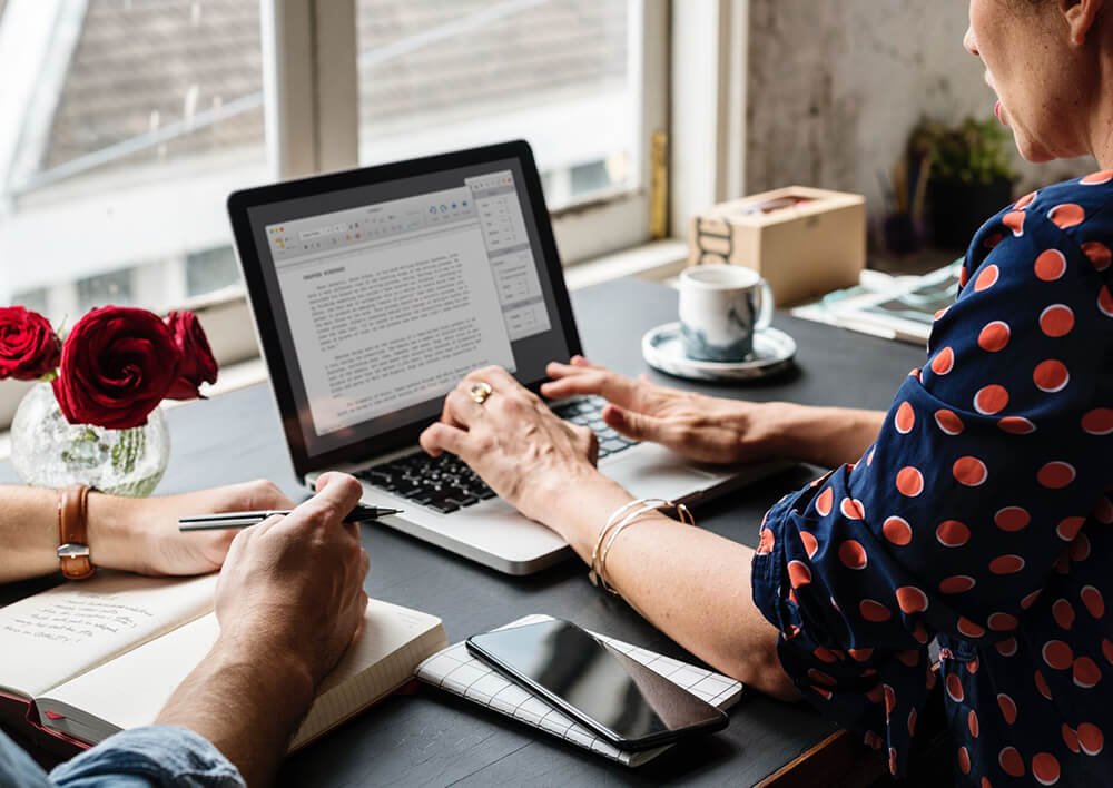 Two people working on a document on a laptop at a café